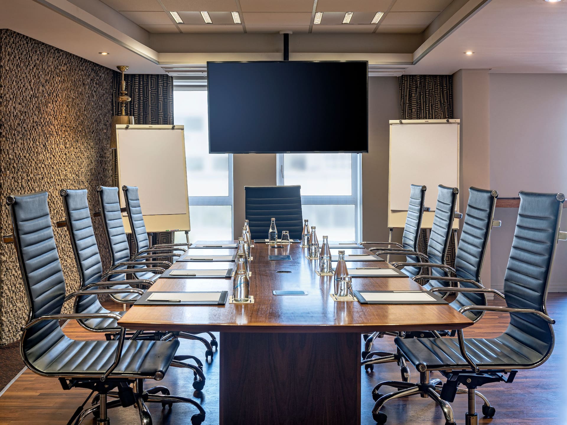 Modern hotel boardroom in Cape Town with a long wooden table, executive leather chairs, large screen, flip charts, and bottled water 