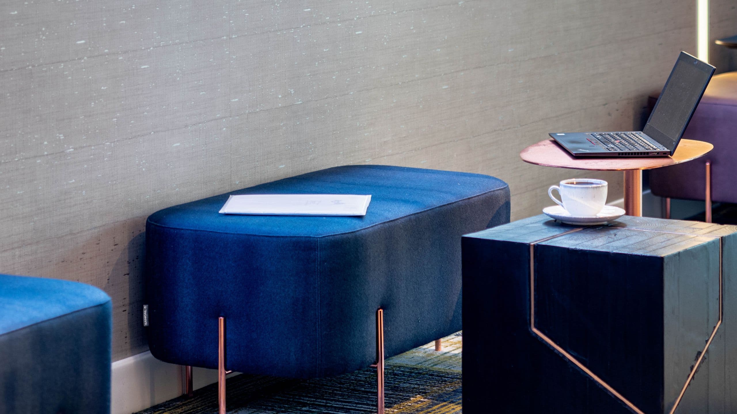 Work area detail with blue ottoman, laptop and cup of coffee