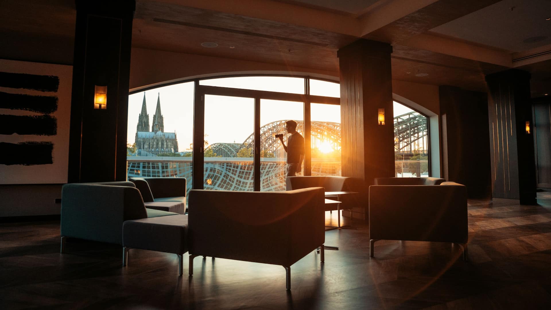 Man stands at the window in the private dining area of Hyatt Regency Cologne and takes a photo of the cathedral and sunset