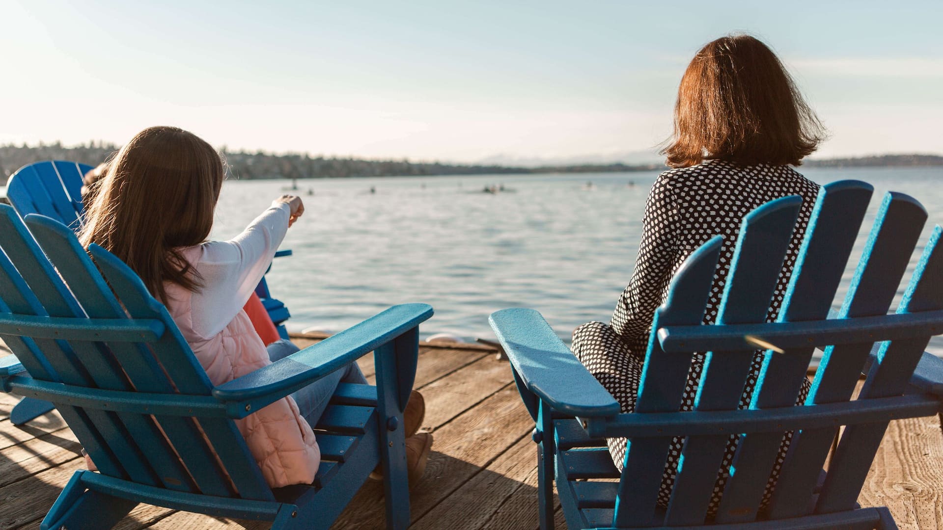 Two people sit in blue Adirondack chairs on a dock by Lake Washington in Seattle.