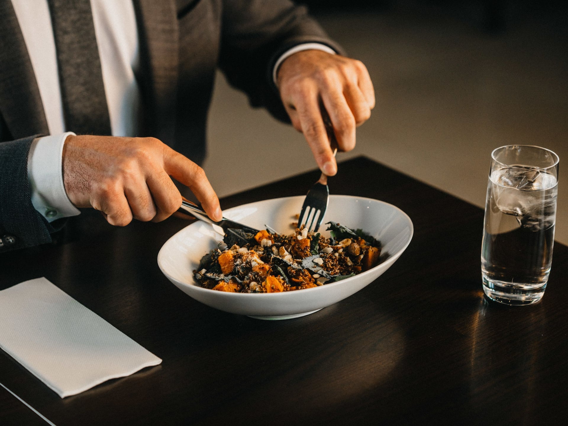 A guest enjoying a meal at the Hyatt Place Amsterdam Airport restaurant, savoring a fresh salad with a fork and knife, accompanied by a glass of water in a modern dining setting.