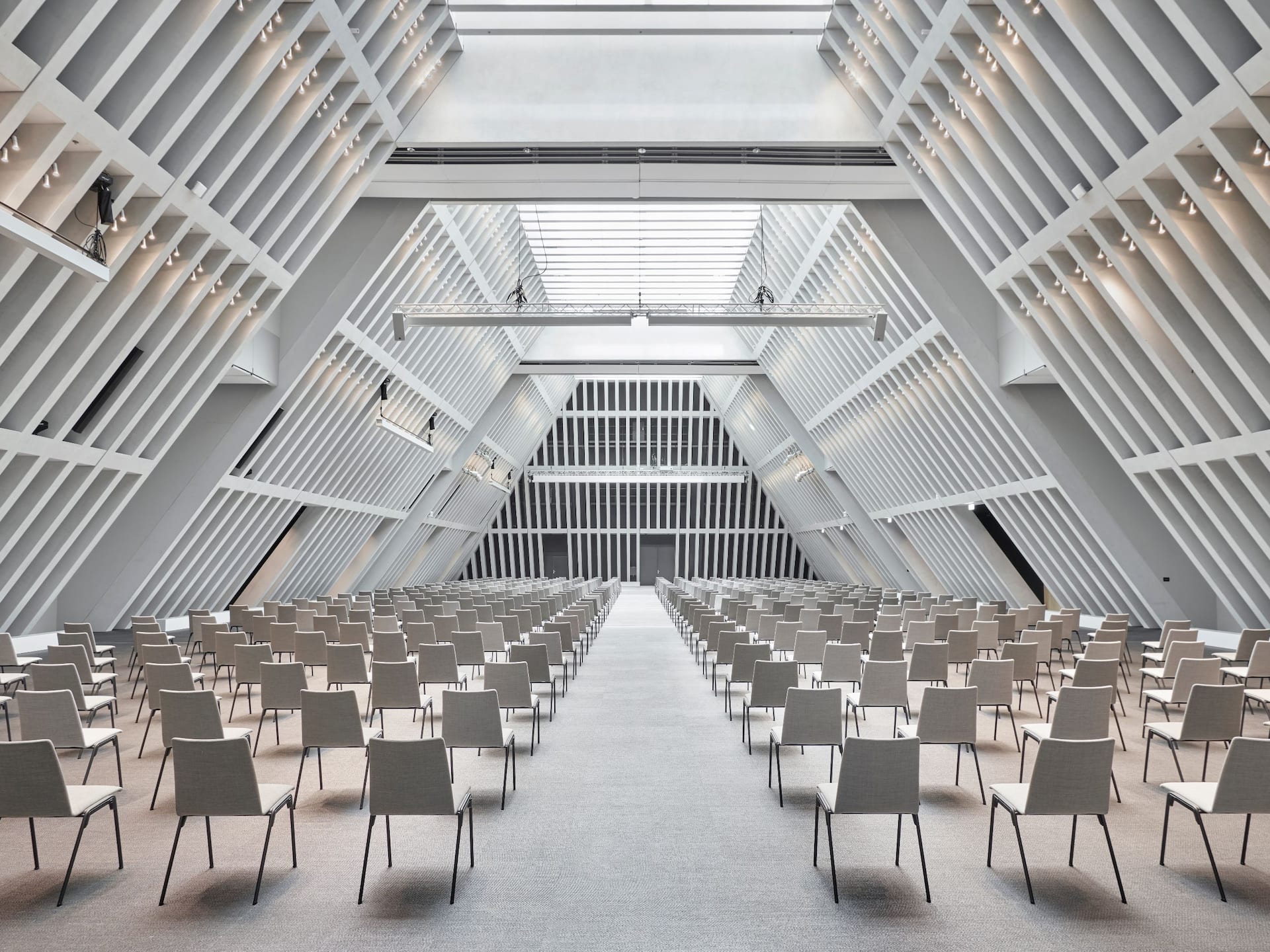The modern The Circle Convention Center Hall with a geometric ceiling, skylight, and minimalist chairs, ideal for meetings and conferences. The venue's clean, airy design offers convenient transport access, creative catering, and event planning services.