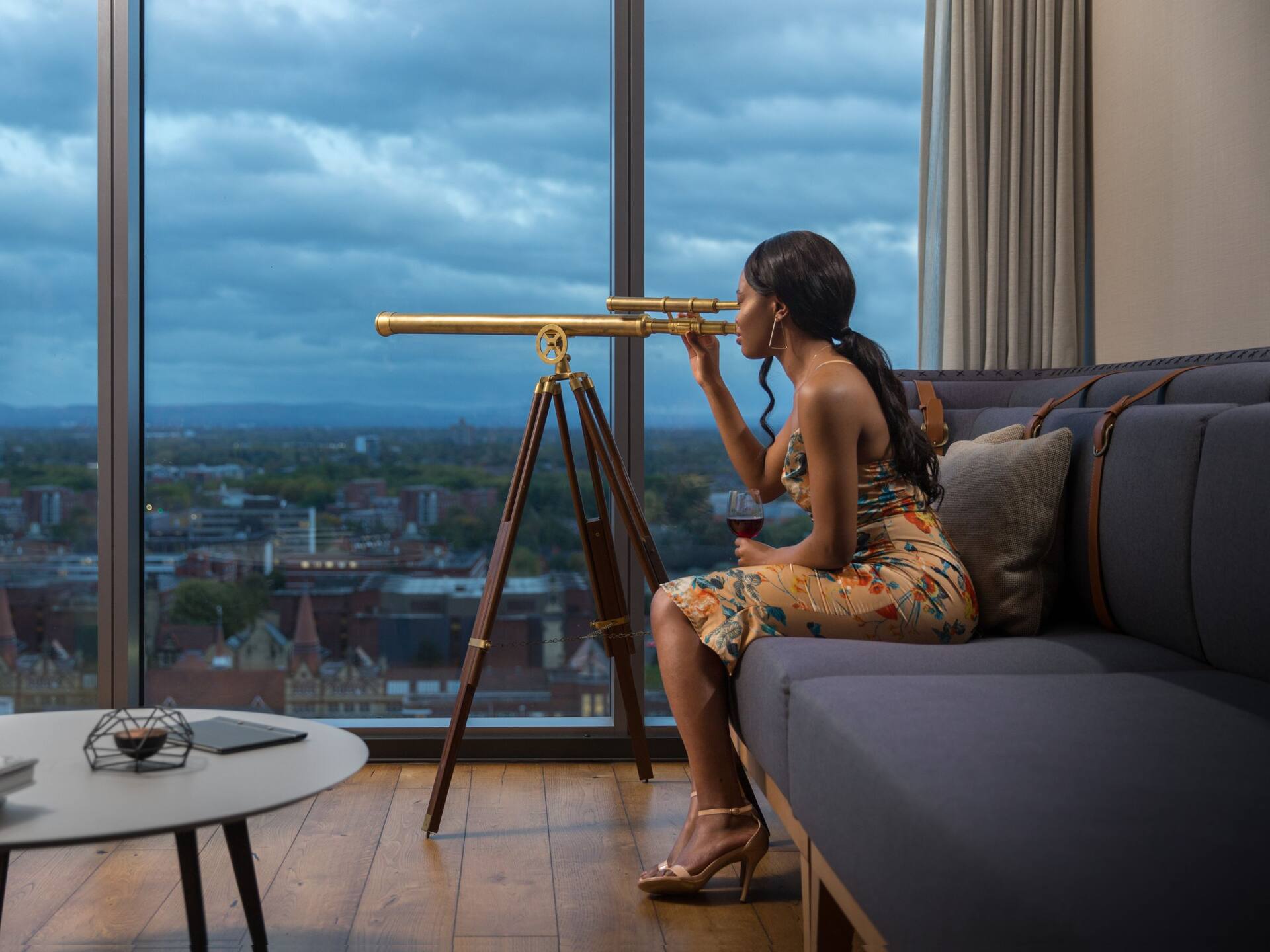 Woman using telescope to view cityscape through floor to celling windows