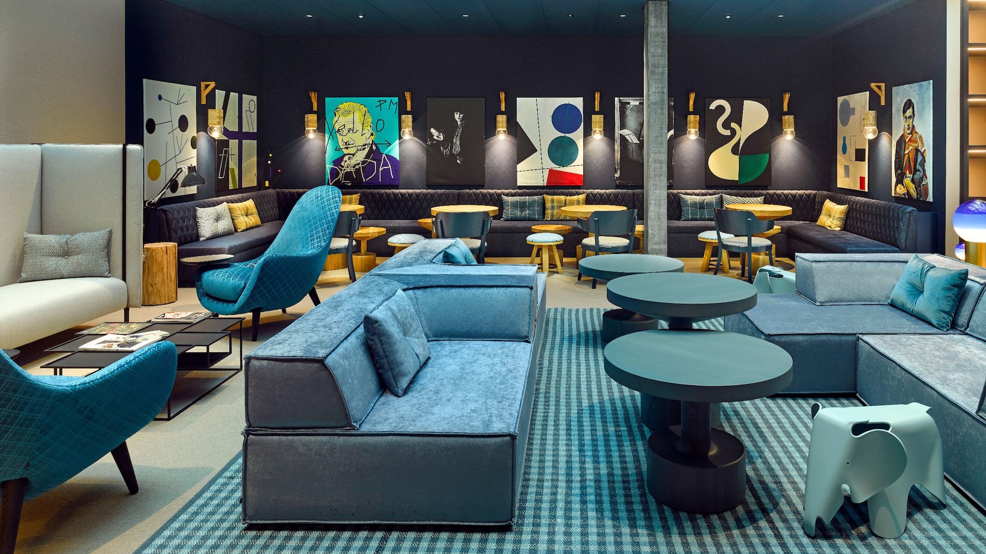 This Zurich hotel lobby features blue velvet seating, patterned chairs, round tables, and Dada-inspired artwork, with warm lighting.