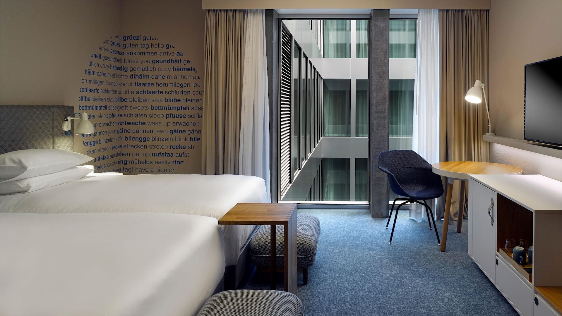 Hotel room in Zurich with two twin beds, a work-desk, a cosy corner sofa and floor-to-ceiling windows with views of the interior courtyard of the Circle
