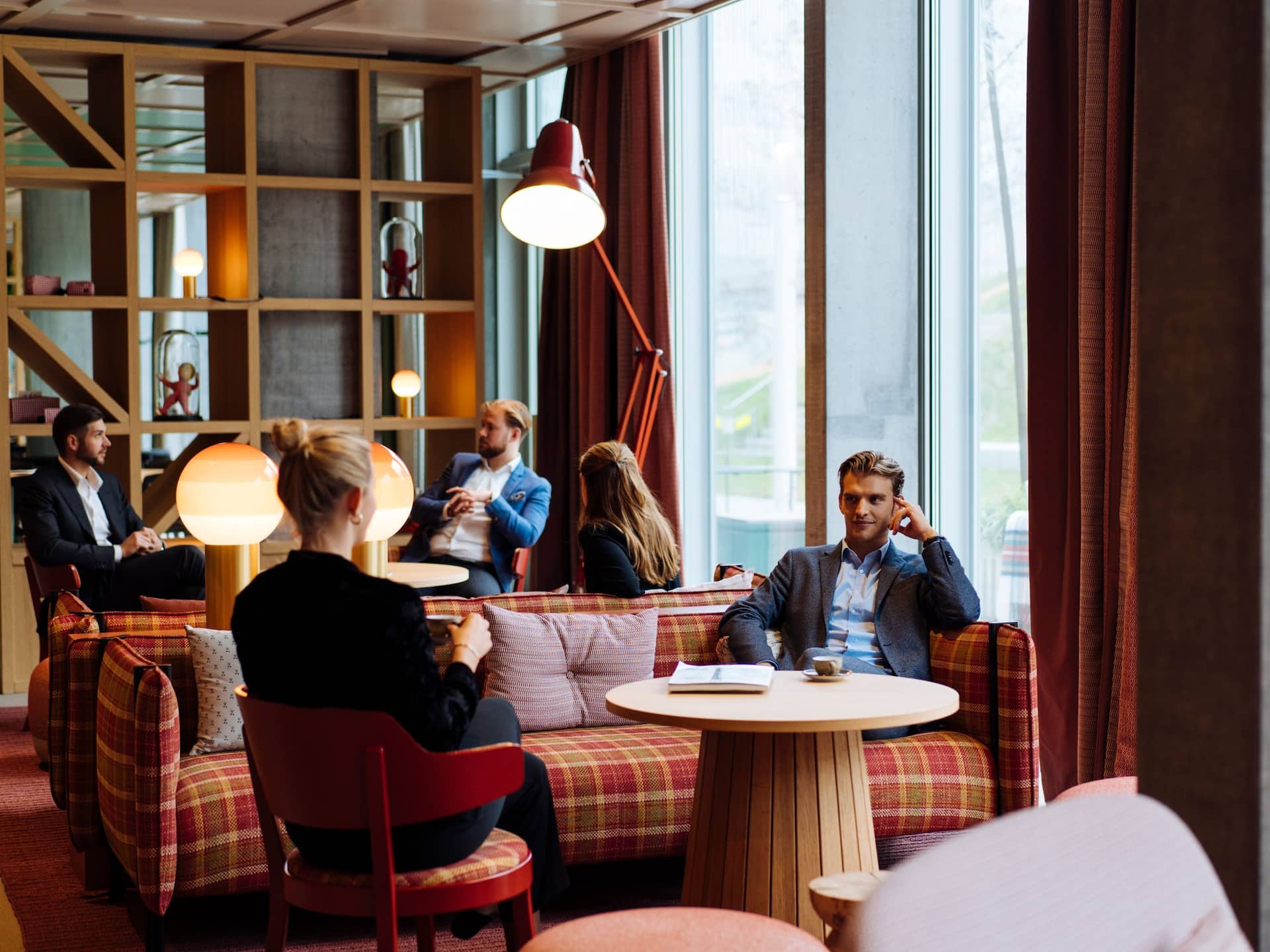 A cozy restaurant lounge at a Zurich hotel with people engaged in conversations, featuring warm lighting, plaid seating, and a modern ambiance.