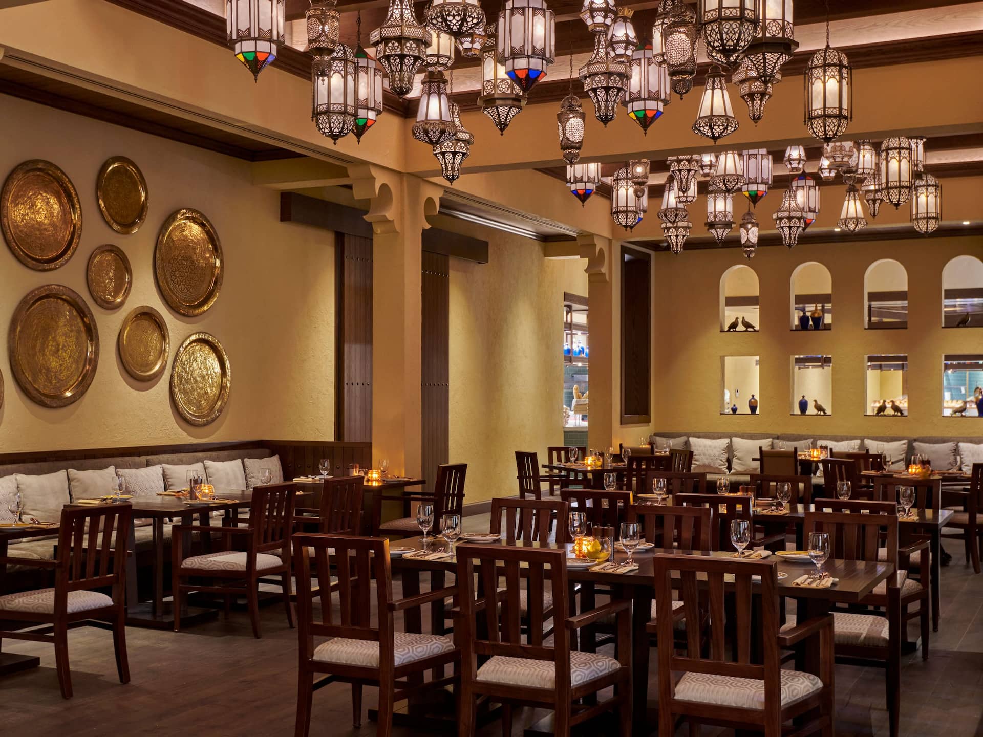 Asmahan at Grand Hyatt Al Khobar an elegant Levantine restaurant featuring warm ambient lighting, intricate hanging lanterns, and traditional gold plated wall decor, The inviting dining space is adorned with wooden furniture