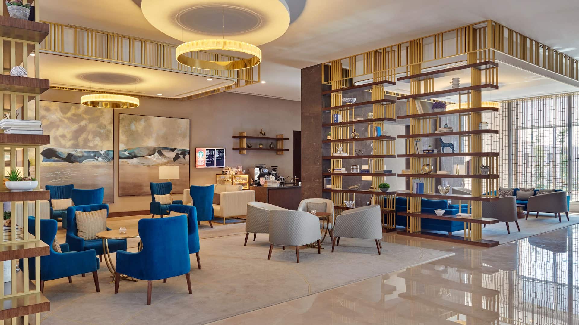 1 of 1 Grandeur Lounge at Grand Hyatt Al Khobar a sophisticated cafe and lounge featuring plush blue and beige seating, elegant gold accented shelving, and warm ambient lighting, The modern space offers a refined setting for coffee