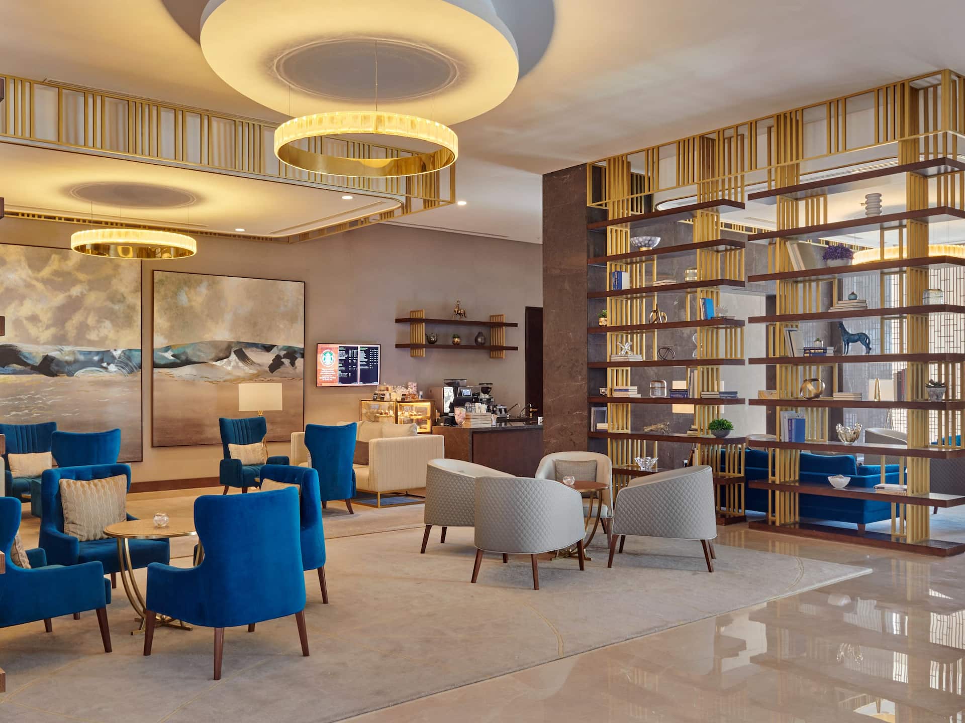 Grandeur Lounge at Grand Hyatt Al Khobar a sophisticated cafe and lounge featuring plush blue and beige seating, elegant gold accented shelving, and warm ambient lighting, The modern space offers a refined setting for coffee