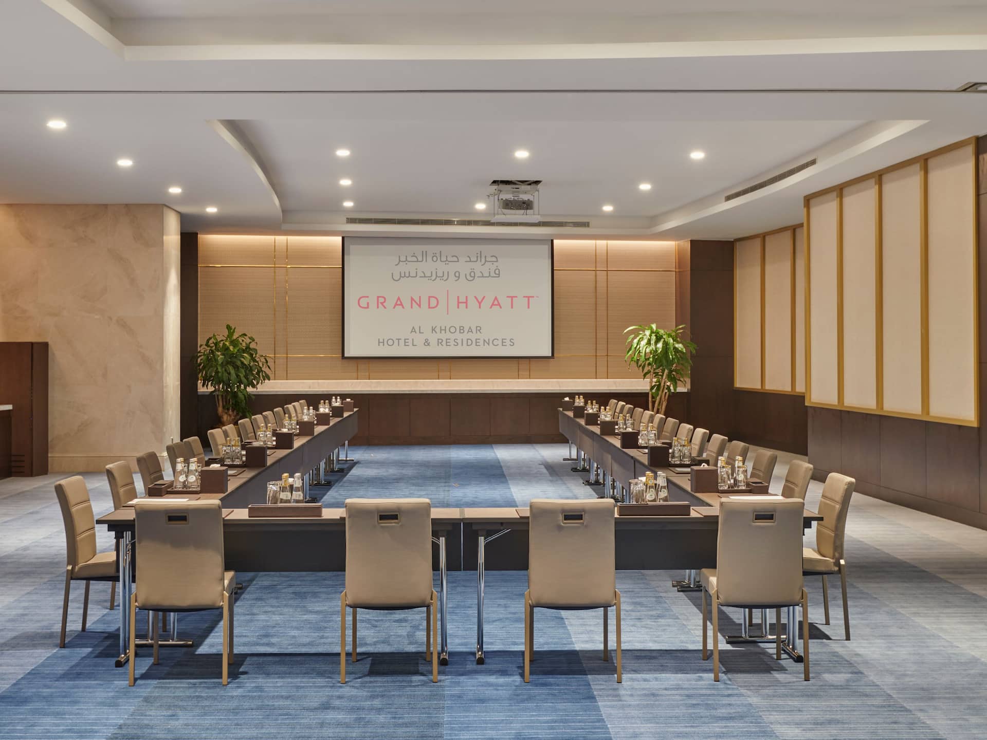 A modern and elegant conference room at Grand Hyatt Al Khobar, set up in a U shape style for business meetings, The room features sleek wooden tables with comfortable beige upholstered chairs