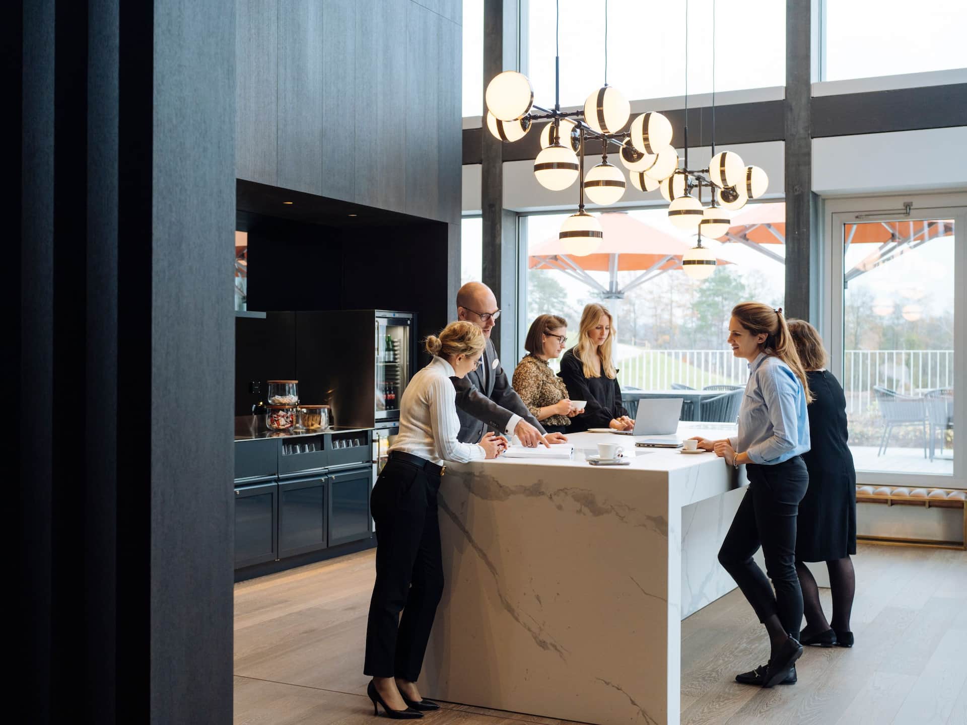 Business professionals gathered around a high marble table in the Regency Club of Hyatt Regency Zurich Airport The Circle, collaborating and brainstorming in an elegant and modern setting.