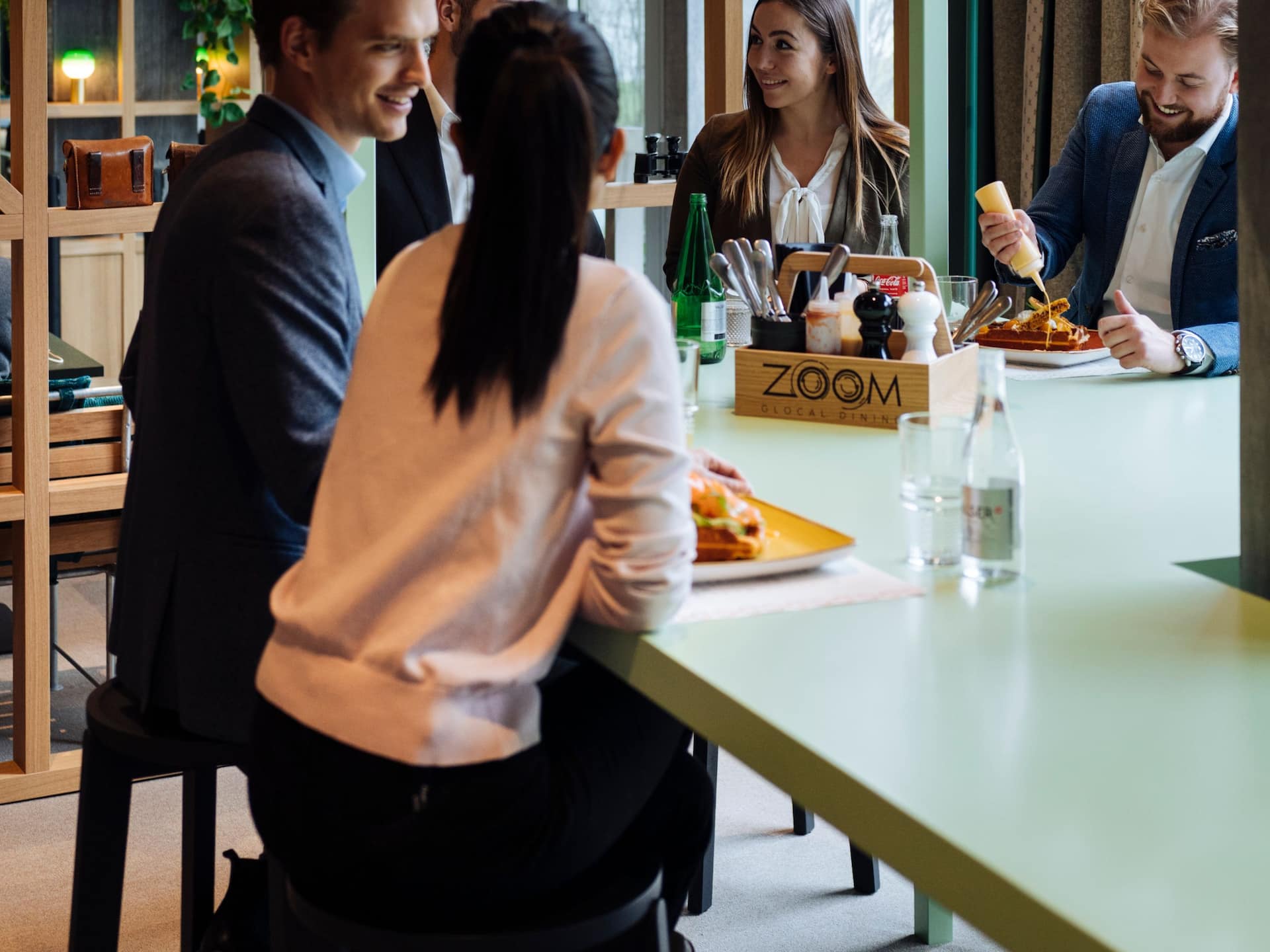 Guests gather around a table enjoying lunch together, sharing a meal in a warm and inviting dining space at a Zurich hotel at Zurich airport.
