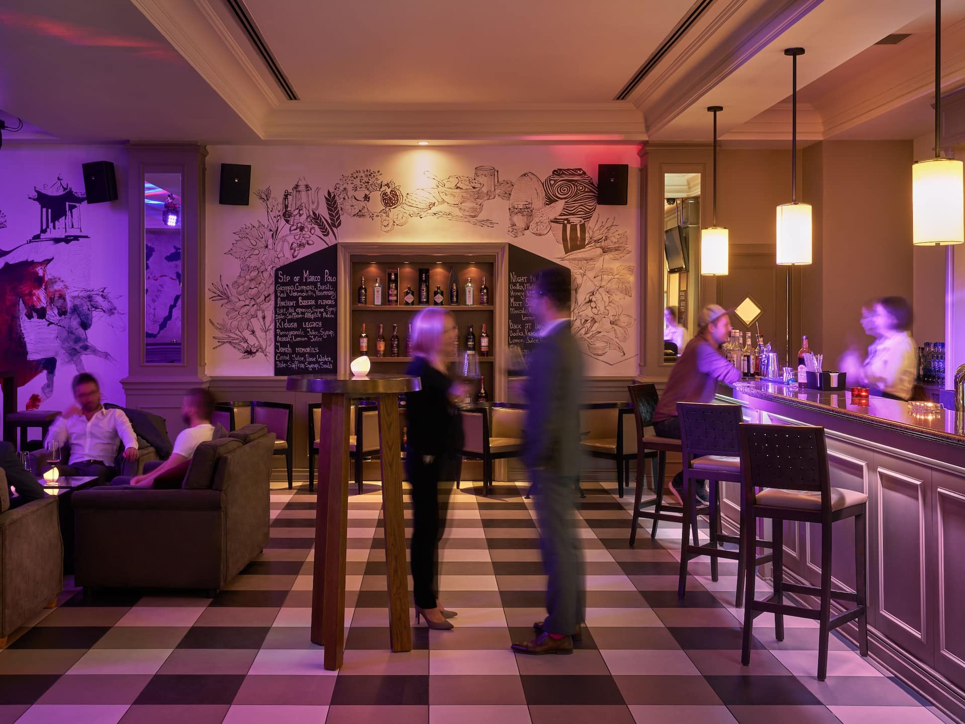 The hotel bar is full of people sitting at the bar, talking, enjoying drinks and socializing in a lively atmosphere