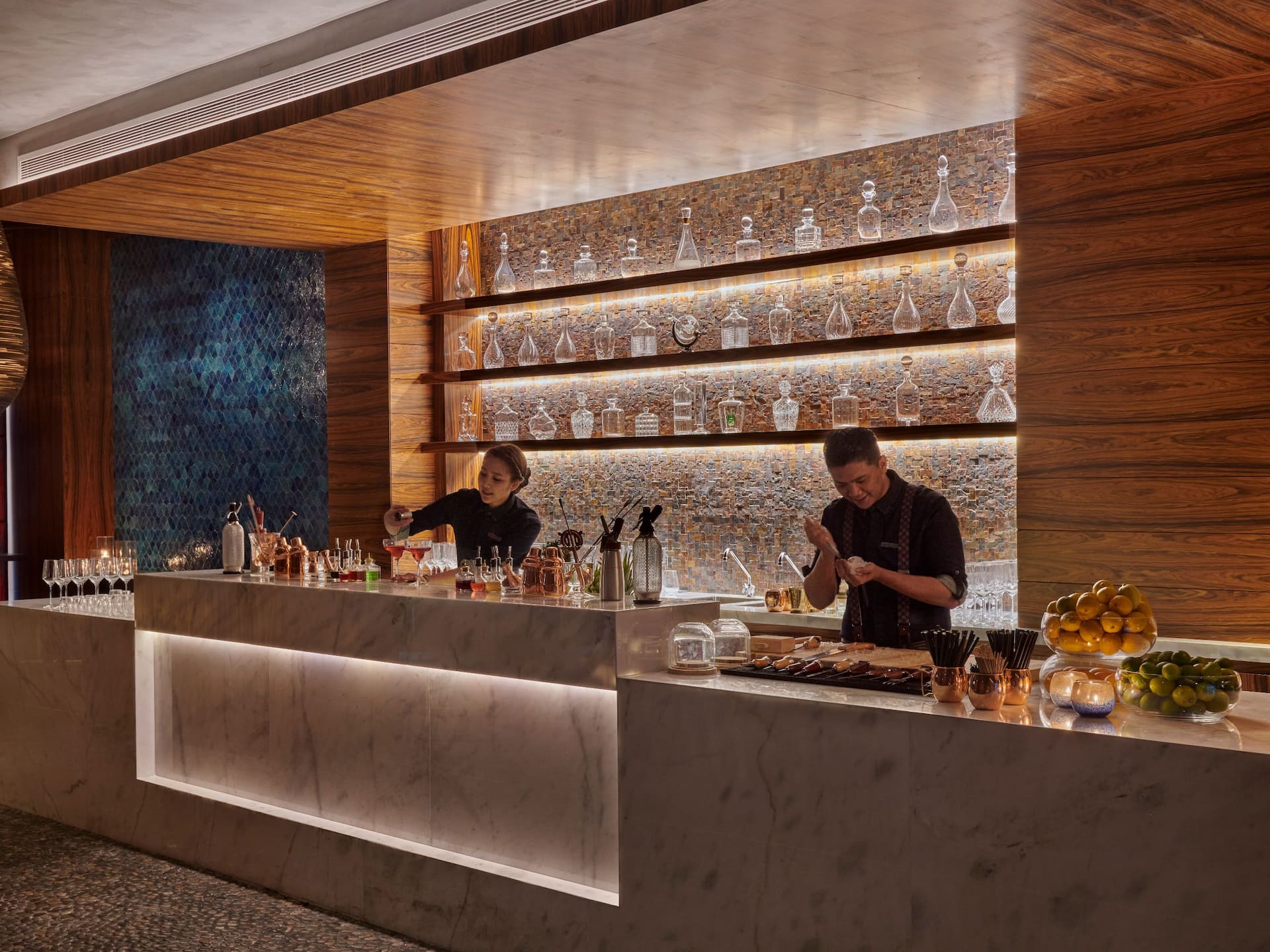 Sakana House at Grand Hyatt Al Khobar a sophisticated multi Asian restaurant with a stylish marble bar, warm ambient lighting, and an elegant display of glassware, Bartenders craft signature drinks and dishes in an intimate setting