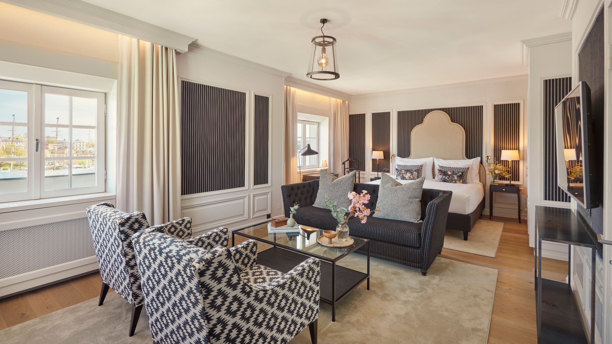 lassic suite with king size bed and a large beige headboard, wallpaper in black and white and a seating area with a sofa, 2 chairs and a coffee table.
