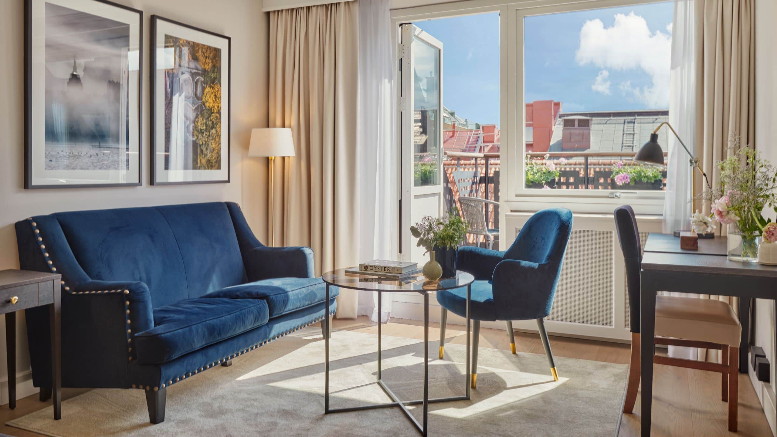 Seating area with furnishers in blue with a glass coffee table in front of a balcony with views over rooftops