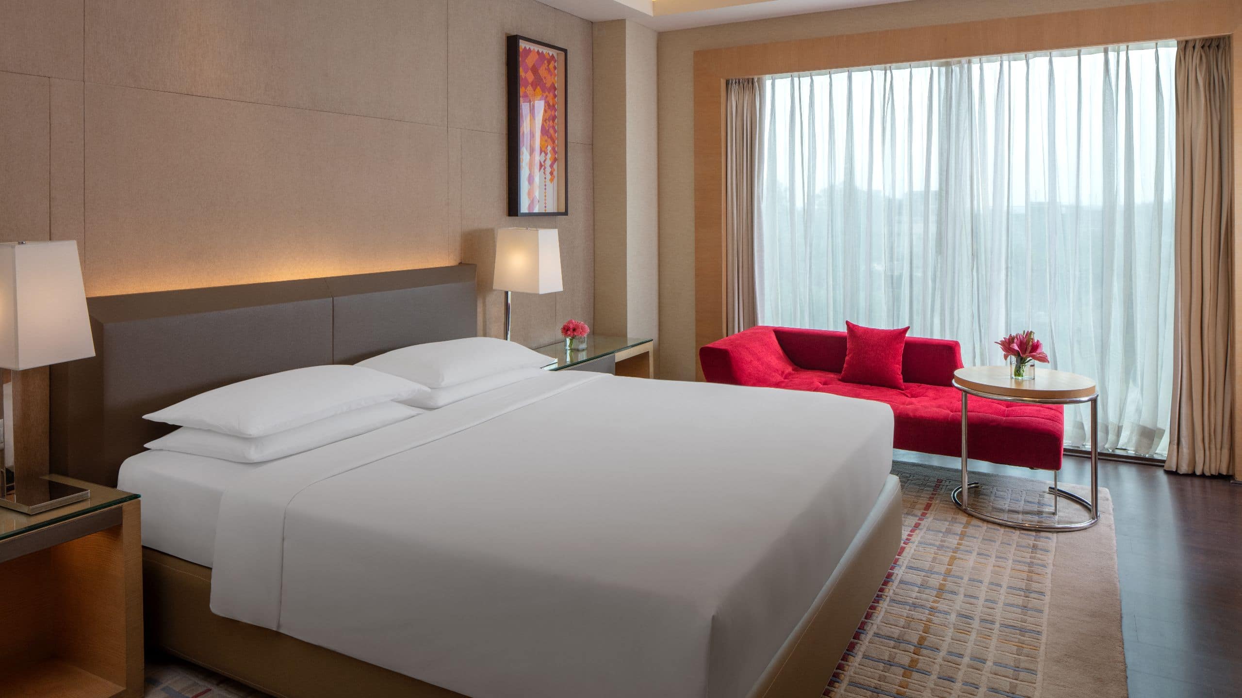King sized bed between nightstands with lamps by window in hotel suite