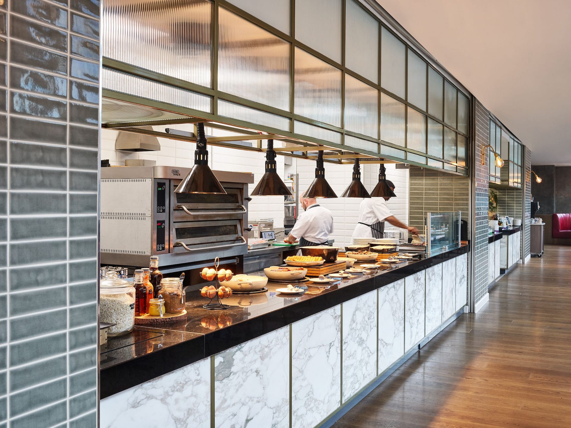 Breakfast buffet with hot items and eggs on a black marble counter and two chefs working in the background.