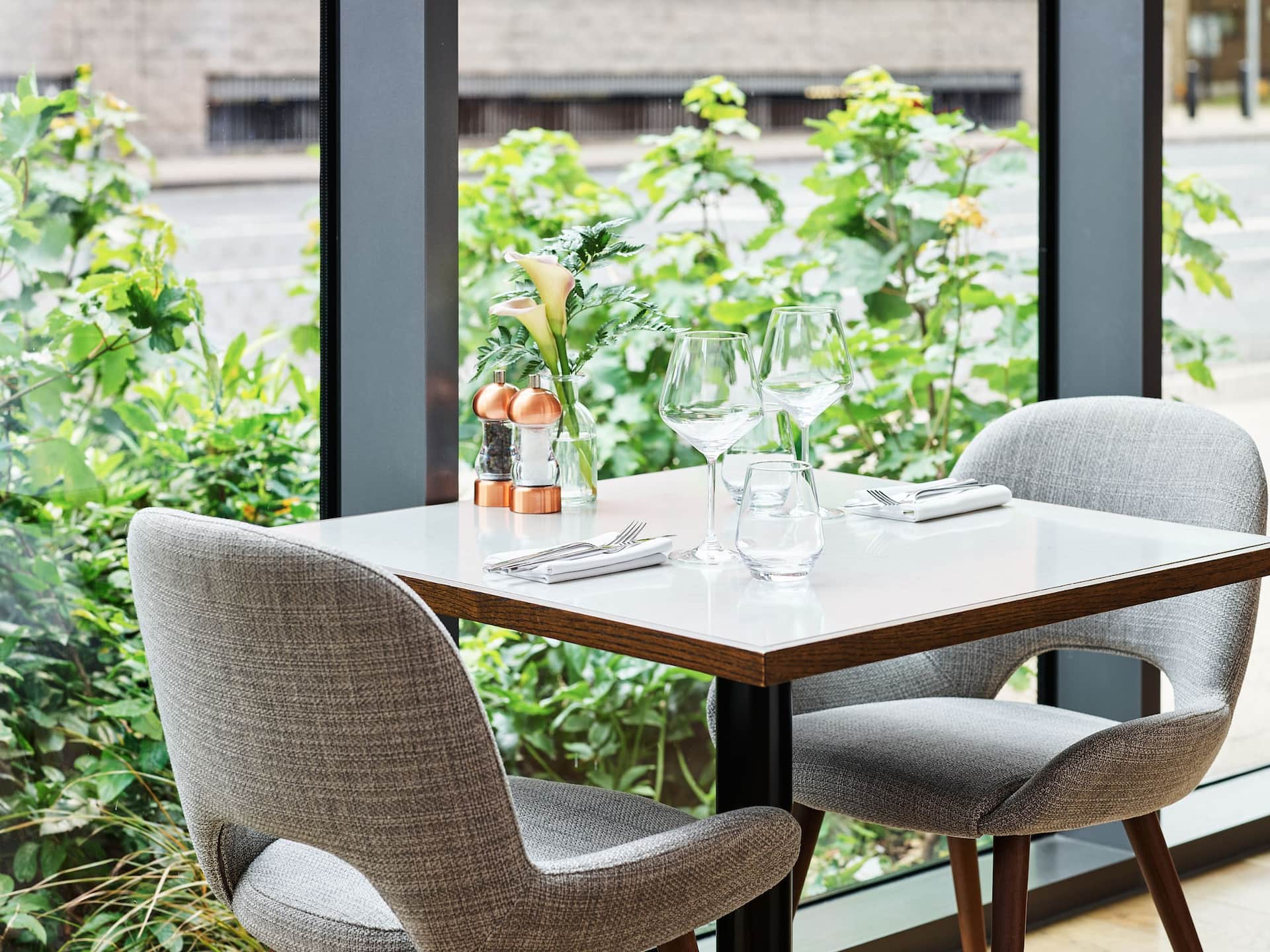Square marble dining table with grey casual chairs against large windows in The Laureate Restaurant