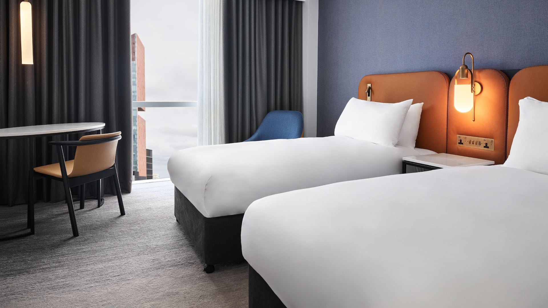 Modern hotel bedroom in grey and blue tones with twin beds, a working desk, a floor-to-ceiling window at Hyatt Hotels 