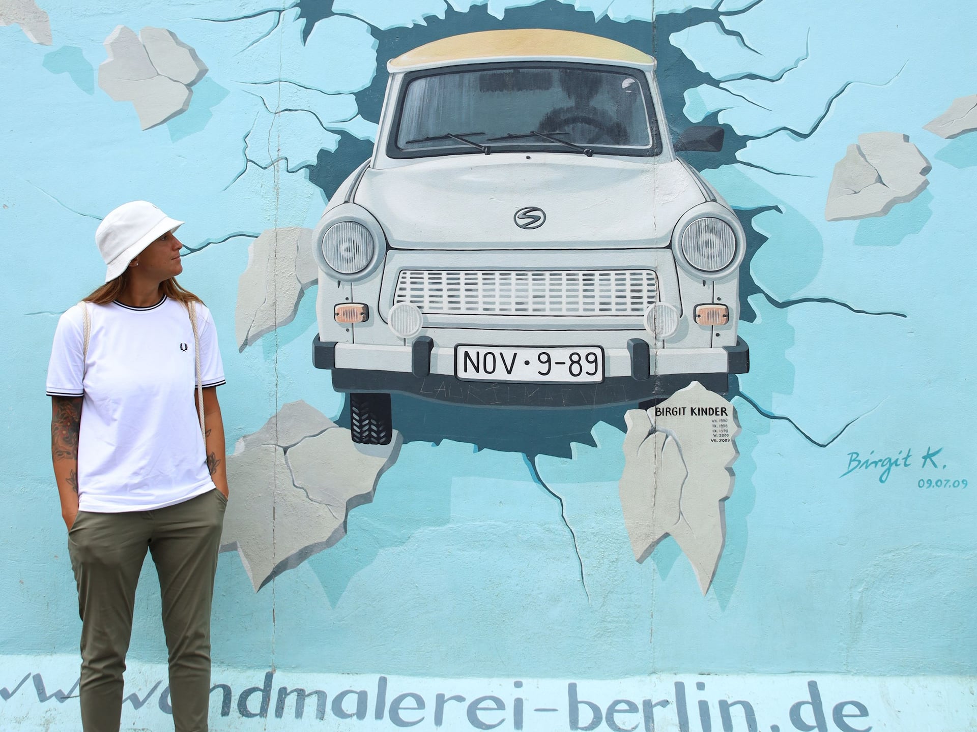 Woman stands in front of a piece of painted Berlin Wall decorated with Trabi car. To be discovered as an incentive activity at Grand Hyatt Berlin