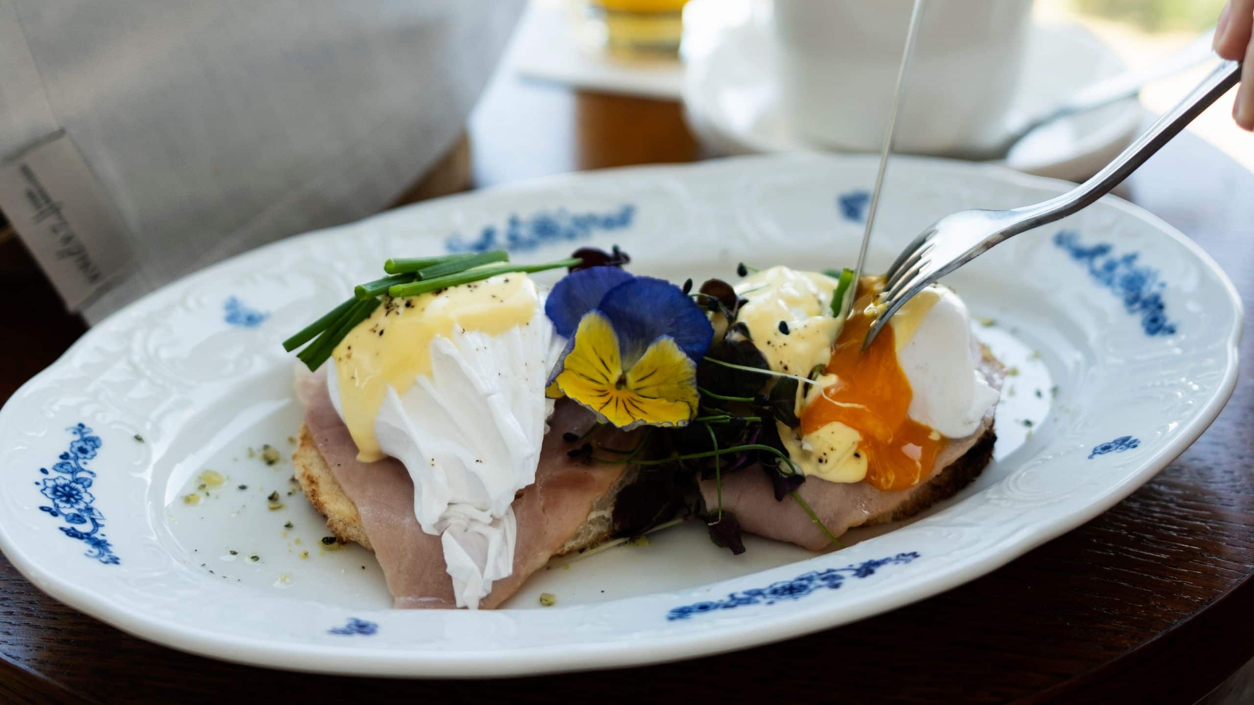 A delicate Eggs Benedict is being sliced, accompanied by freshly brewed coffee and orange juice