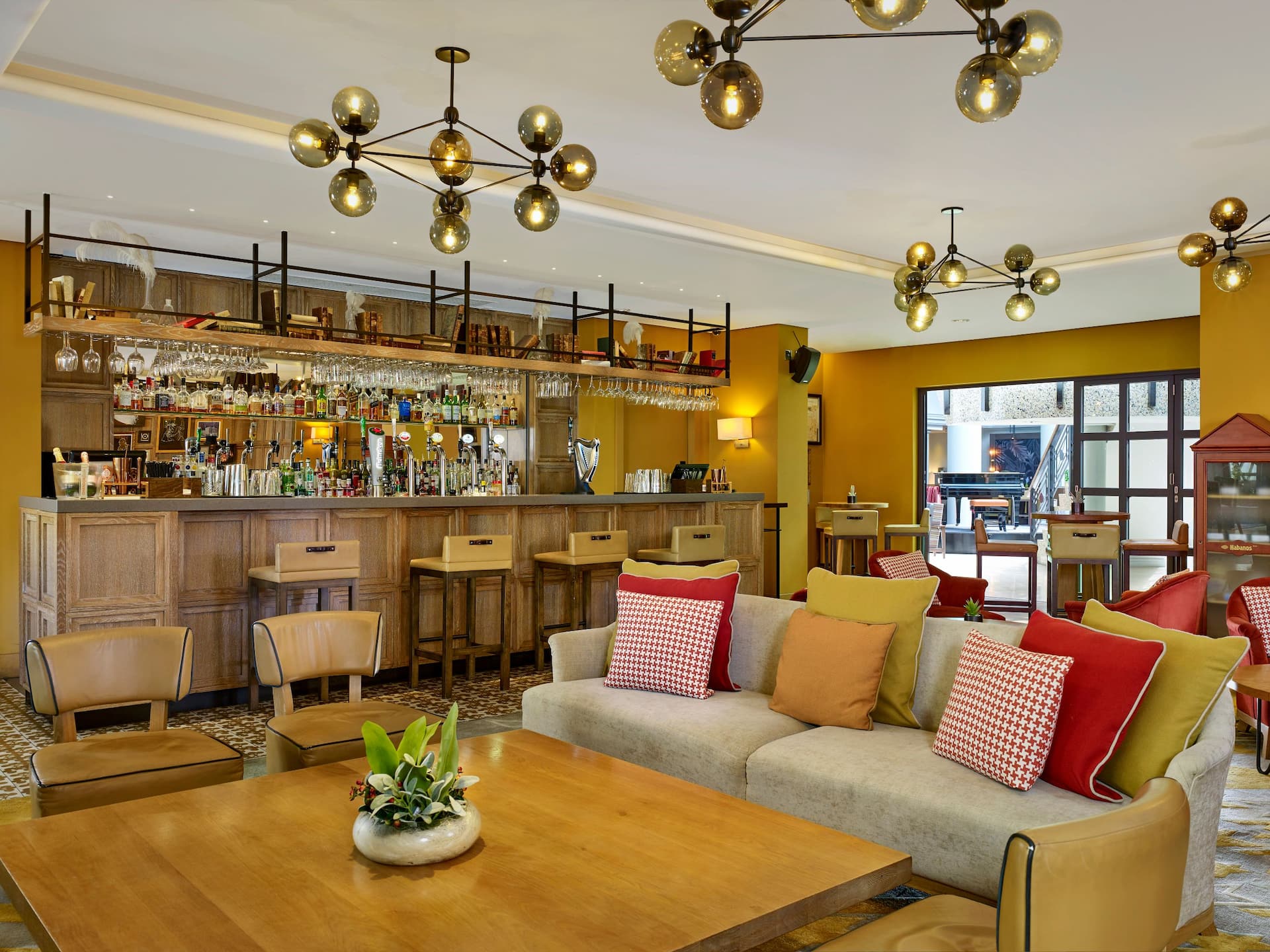 A comfortable sofa with colourful cushions at the Gentleman & Scholar Pub in Birmingham, with the pub bar presenting several bottles and glasses.