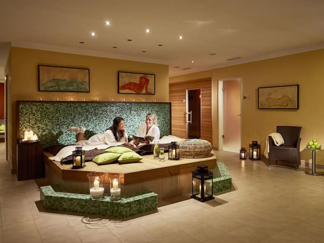 Two women relaxing on a lounger in a hotel at the Nürburgring in a room with mosaic design and spa area