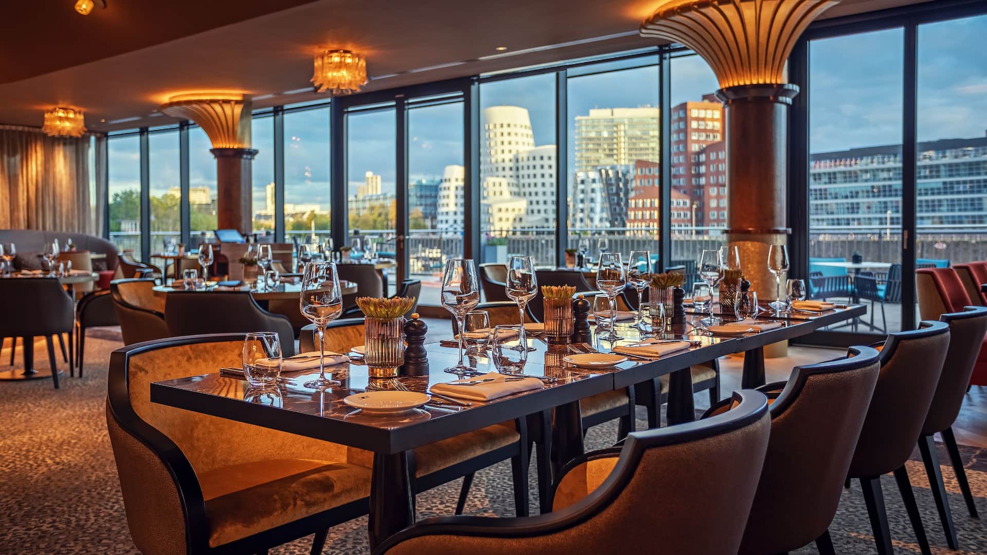 DOX Restaurant at the Hyatt Regency Dusseldorf, in a shimmering gold style, dark covered marble look tables, comfortable armchairs and a view of the MediaHarbour