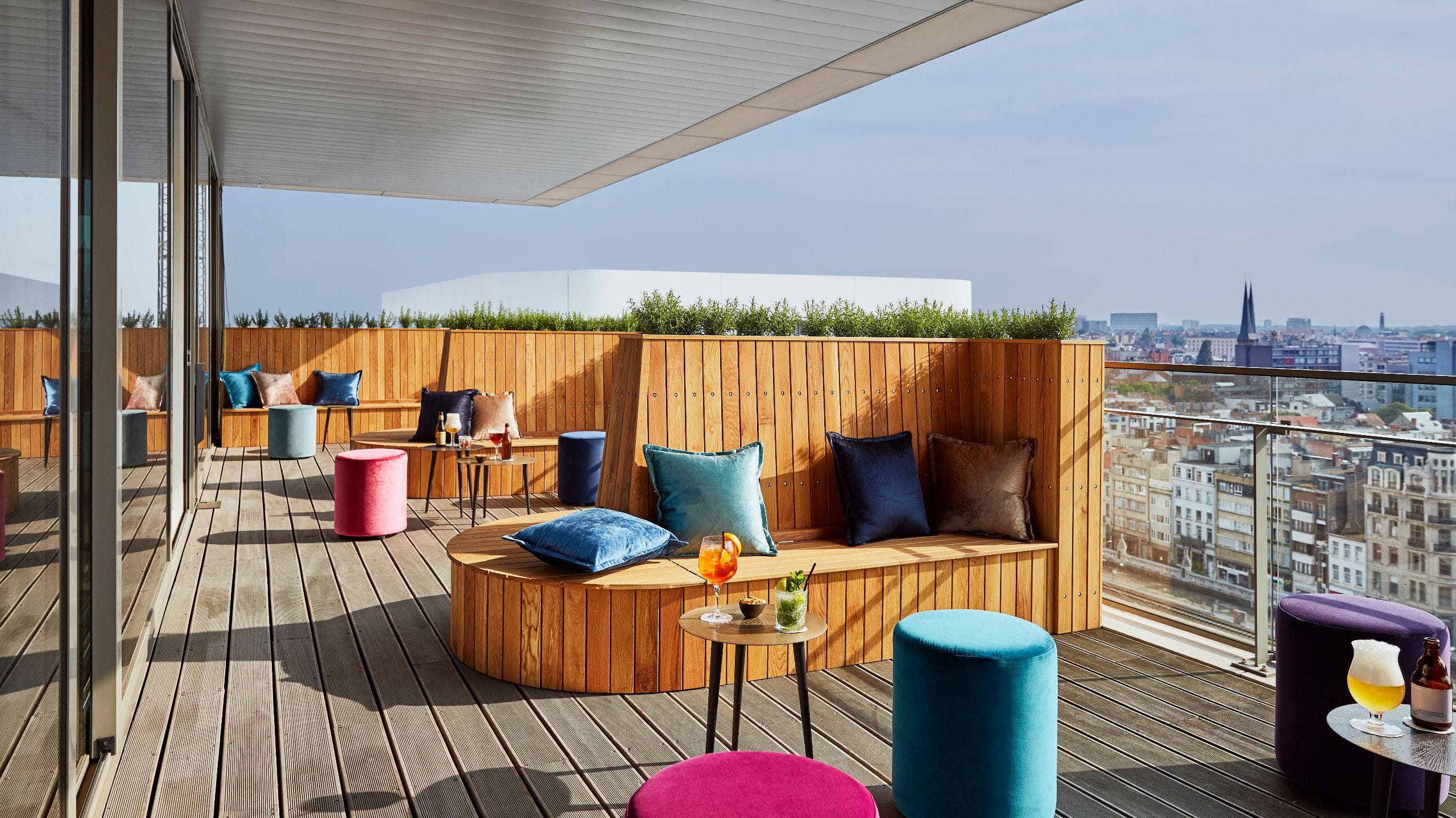 Sky Lounge des Lindner Hotel Antwerpen mit moderner Terrasse, Holzbank, bunten Polstern und Stadtblick