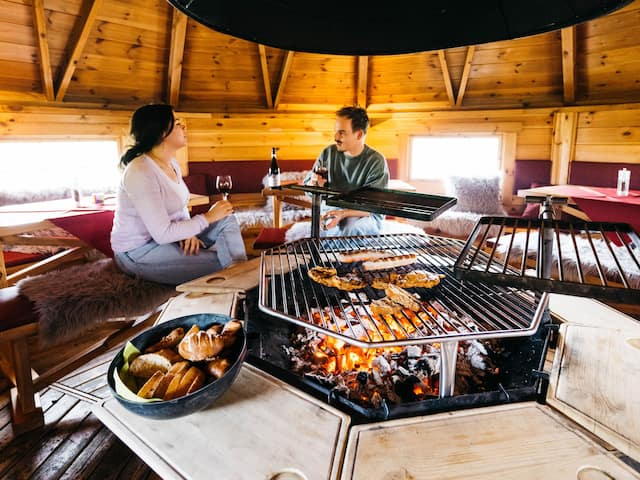 A romantic room with two people drinking wine, featuring an open fire and grill area in a hotel at the Nürburgring.