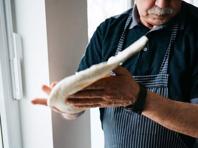 A pizza baker with a watch and a mustache in a hotel at the Nürburgring preparing a pizza.