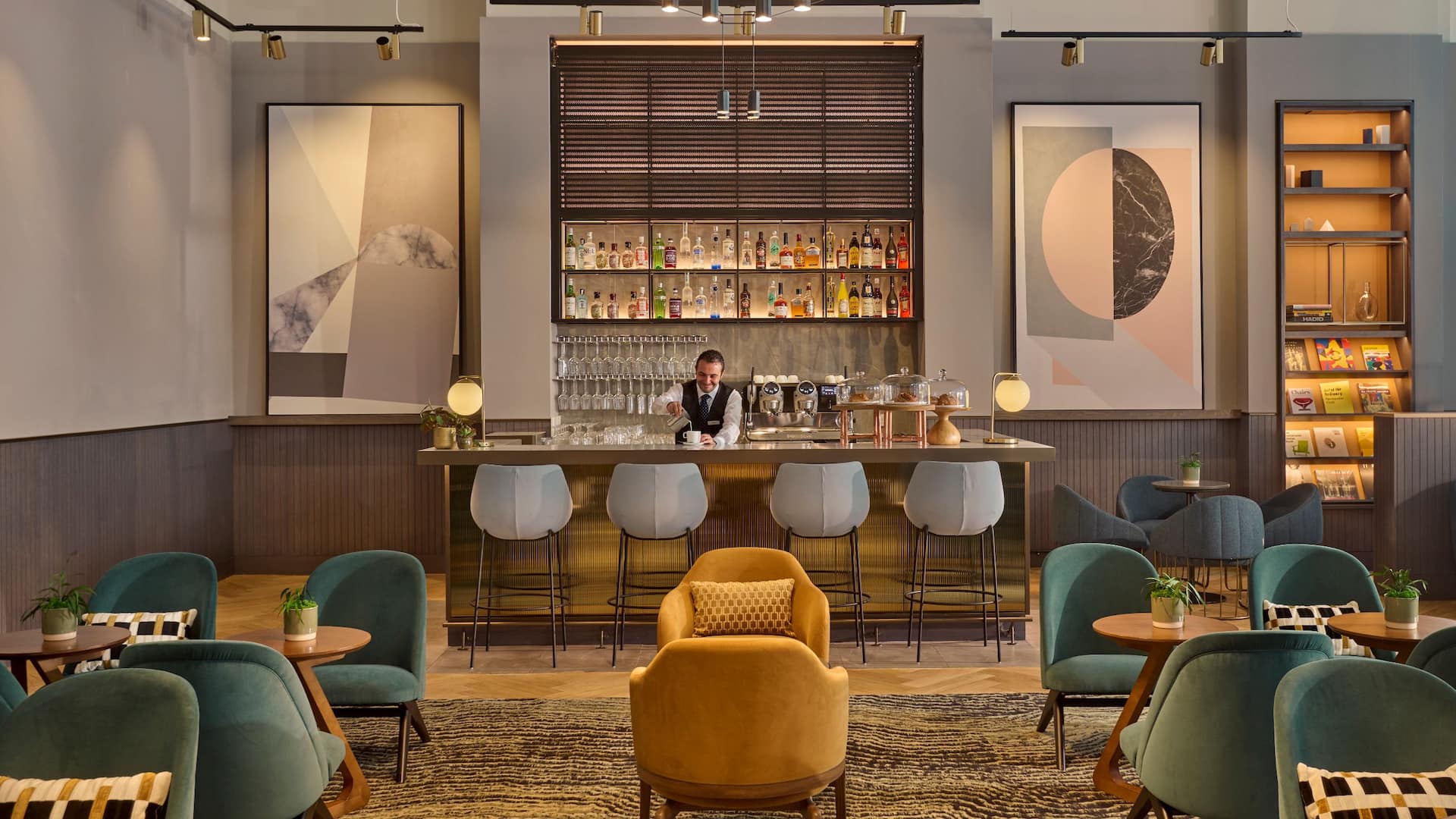 Seating area of the lounge at Hyatt Regency Blackfriars with yellow and blue sofas, wooden tables and a bar for all day dining with grey chairs
