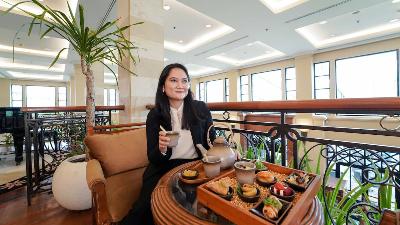 Woman enjoying afternoon tea at Paseban Lounge, Hyatt Regency Yogyakarta