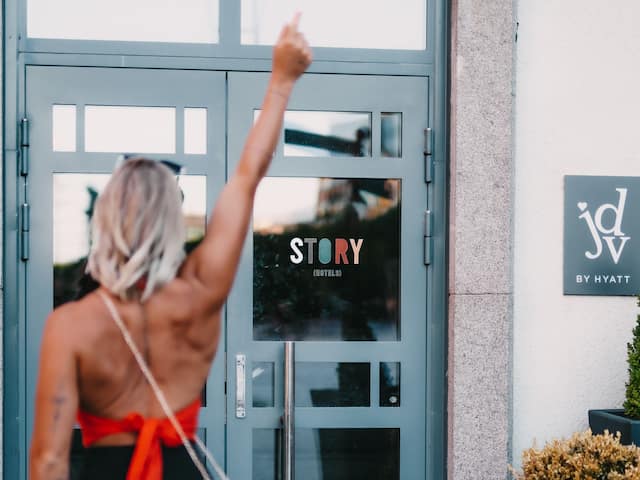 Woman arriving to Story Hotel Signalfabriken in Sundbyberg, in front of the main entrance showing both Story Hotels and Jdv by Hyatt brand logotypes on building