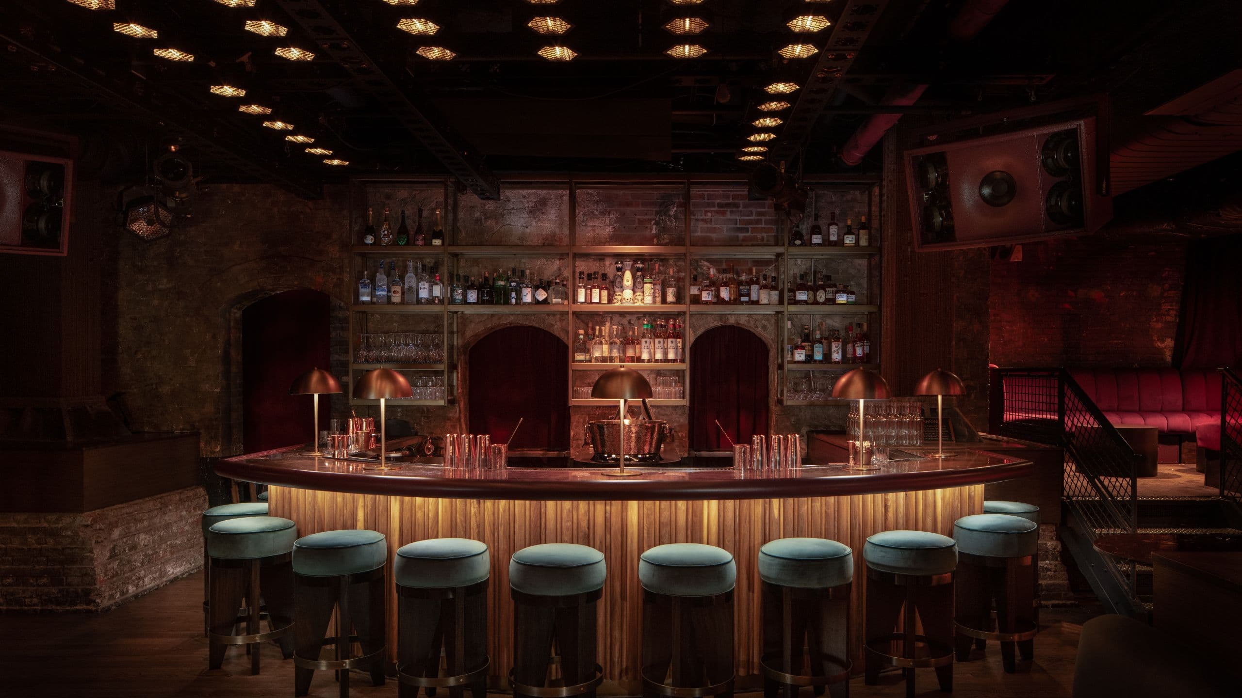 A bar shelving built against an exposed brick wall with a curved bar with stools in the Laissezfaire bar