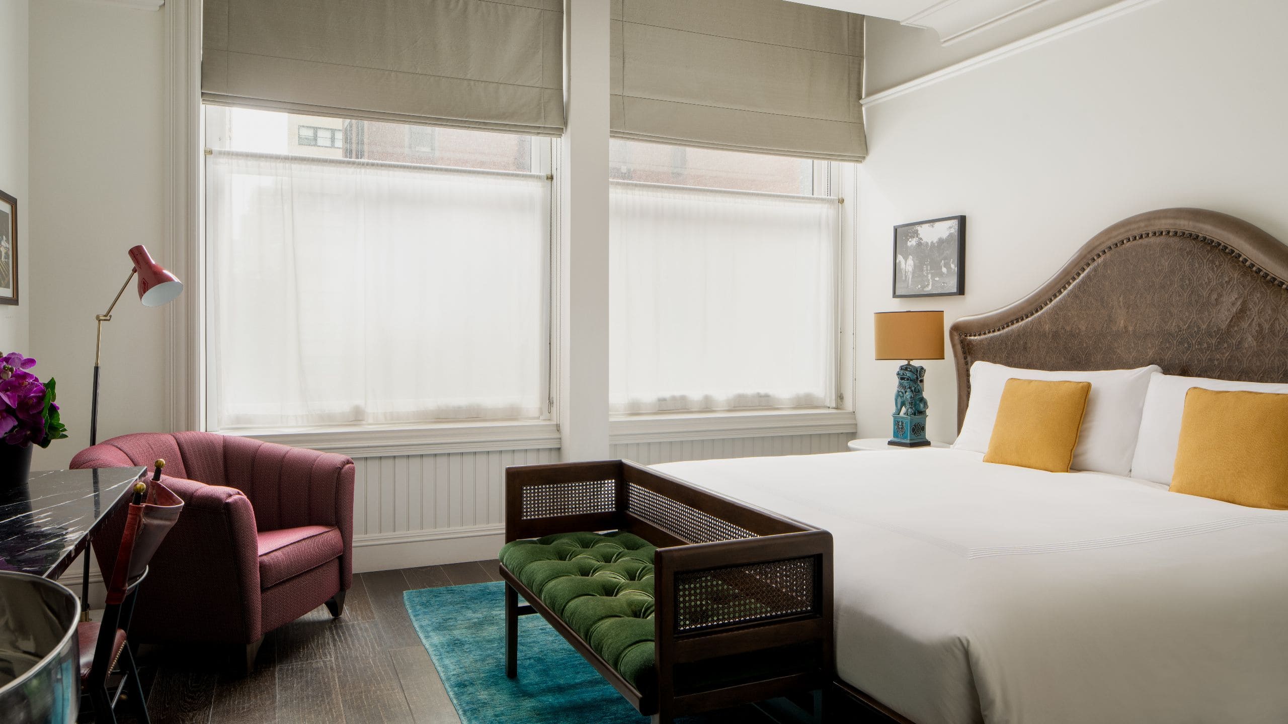 King bed with a bench at the foot of the bed, a side chair and two windows