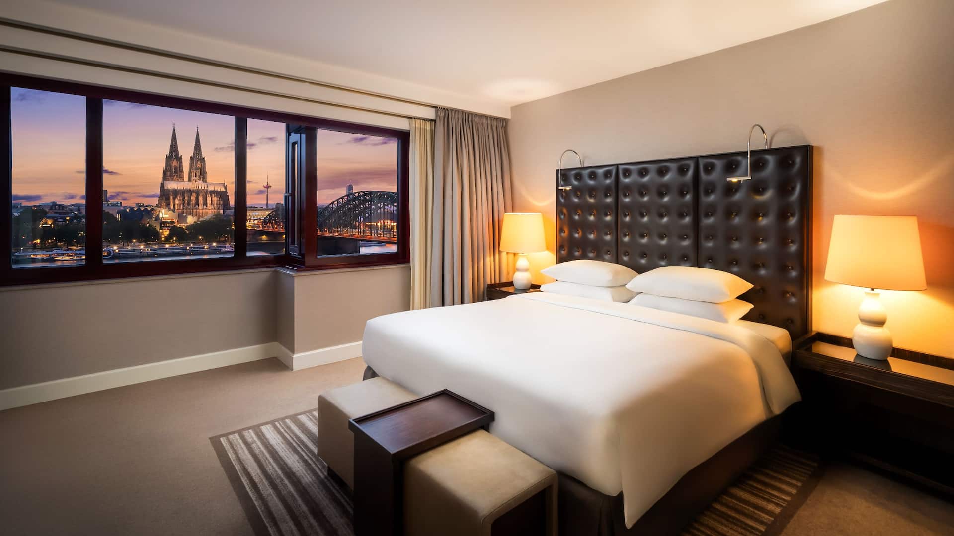 Spacious bedroom of the Executive Suite at Hyatt Regency Cologne with view of the cathedral at dusk