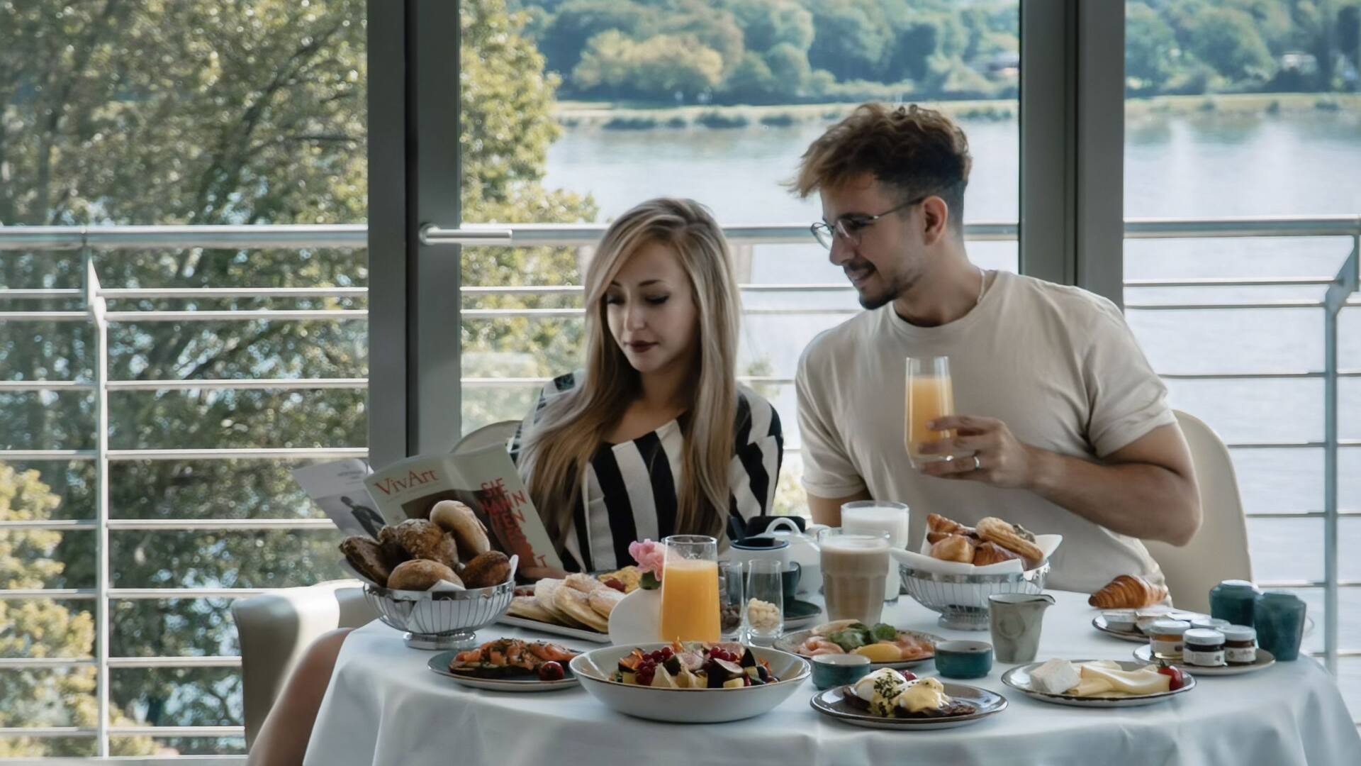 Paar nimmt auf dem Zimmer mit Rheinblick sein bestelltes Roomservice Frühstück im Hyatt Regency Mainz ein.