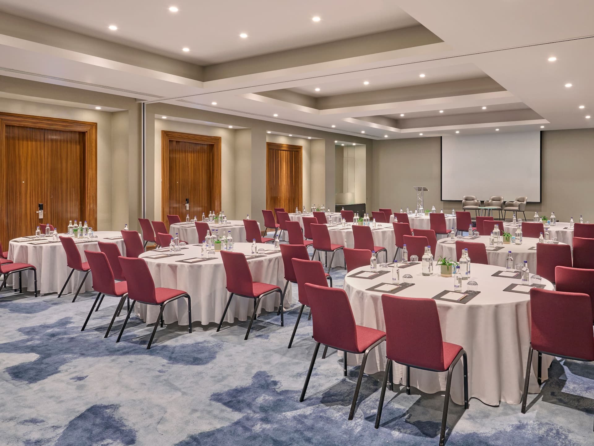 Event space at Hyatt Regency London with round meeting table with table cloths, glasses and papers, red chairs and a blue carpet