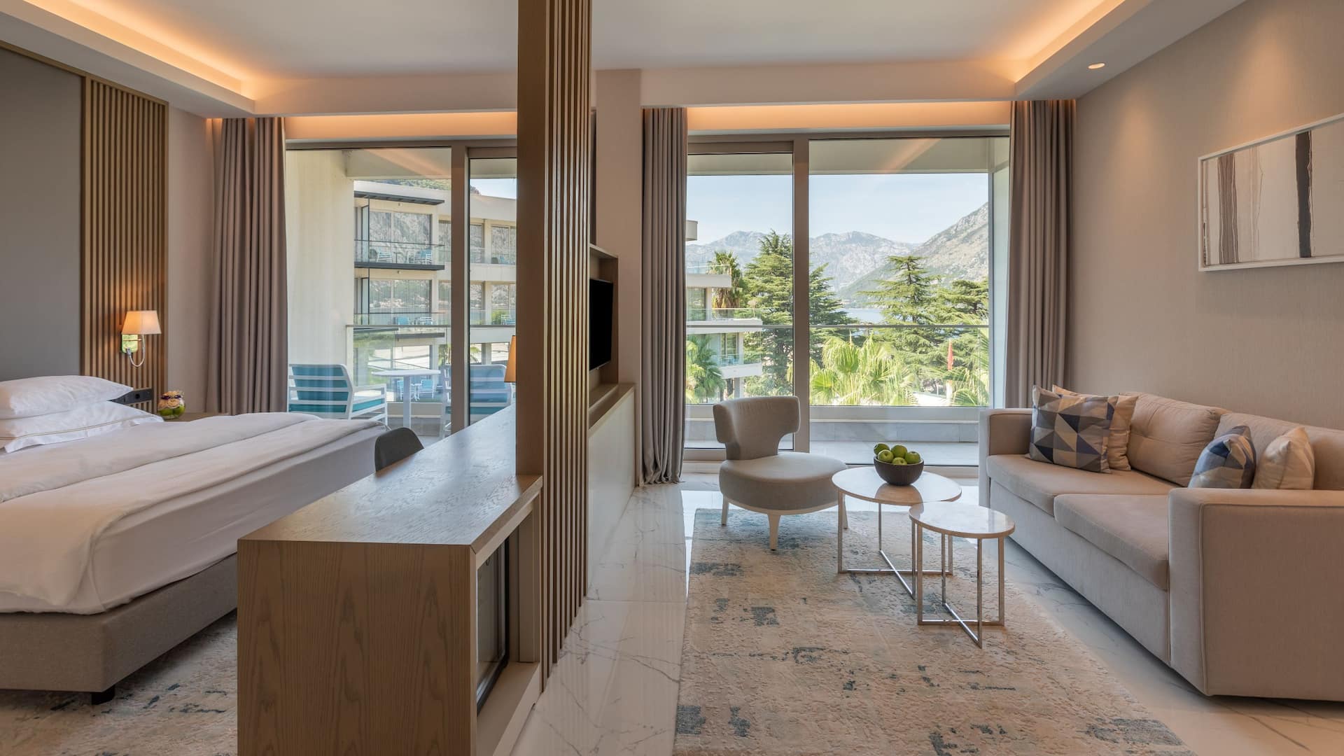 1 de 4 Premium suite at Hyatt Regency Kotor Bay with a king bed, stylish living area, and a private balcony overlooking palm trees and mountains.