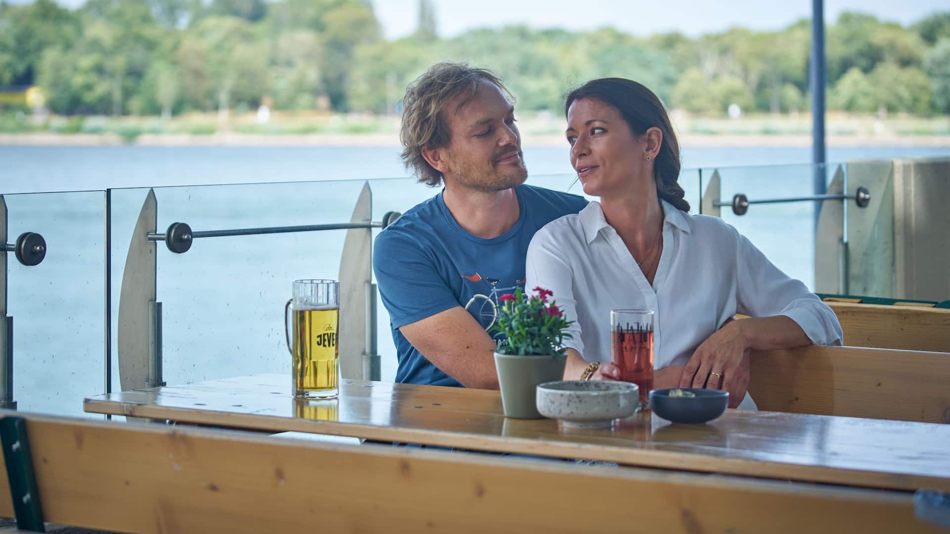 Couple sitting in beer garden Hafenbar looking at each other with Rhine in the back
