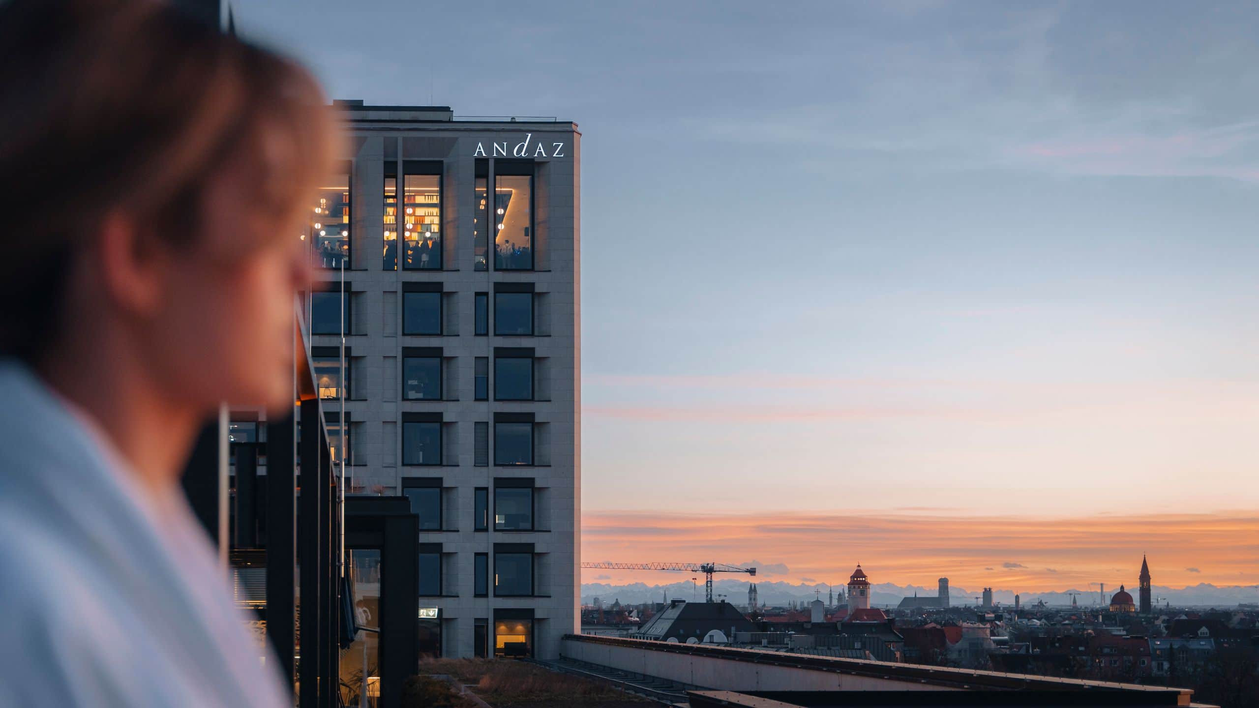 A woman relaxes during day spa at sunset on the rooftop of the Andaz Spa terrace, with the Andaz Munich hotel