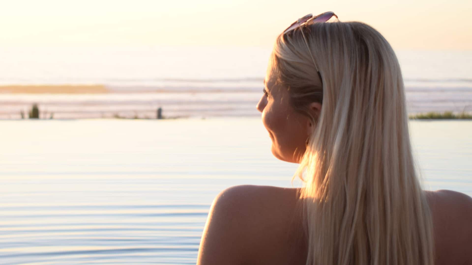 Girl relaxing in the pool, gazing at the sunset with vibrant colors reflecting on  the water.