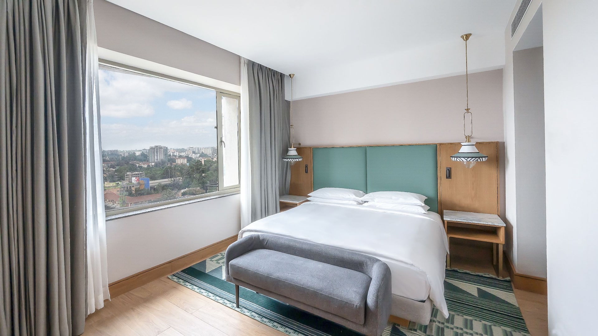 Executive Suite at Hyatt Regency Nairobi Westlands, featuring a king-sized bed, cushioned bench, modern décor and large panoramic windows with a view of the city.