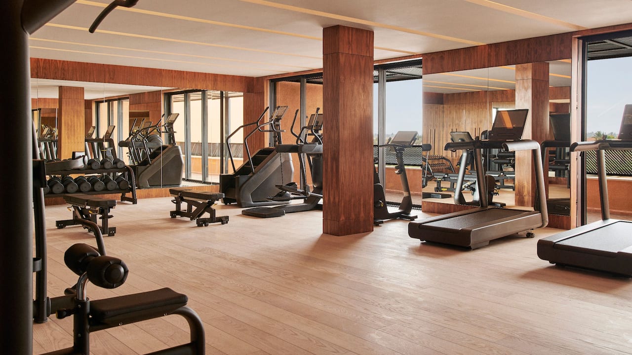 Modern gym interior at the Park Hyatt Marrakech, featuring various exercise machines like treadmills and ellipticals, wooden floors, and mirrored walls.