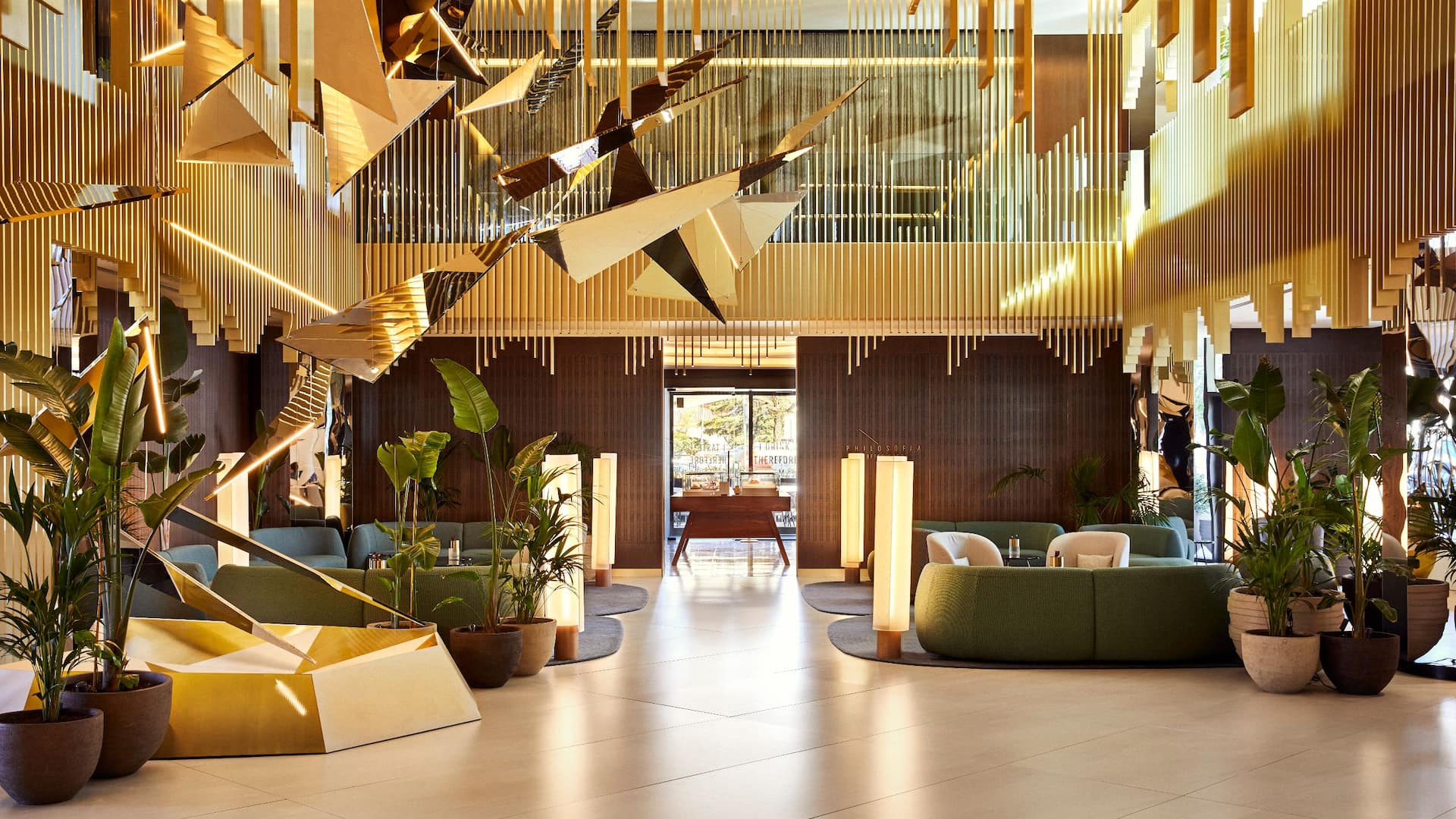 Luxury hotel lobby with geometric ceiling decorations, vertical wood paneling, and elegant furnishings, with a person walking across the space.