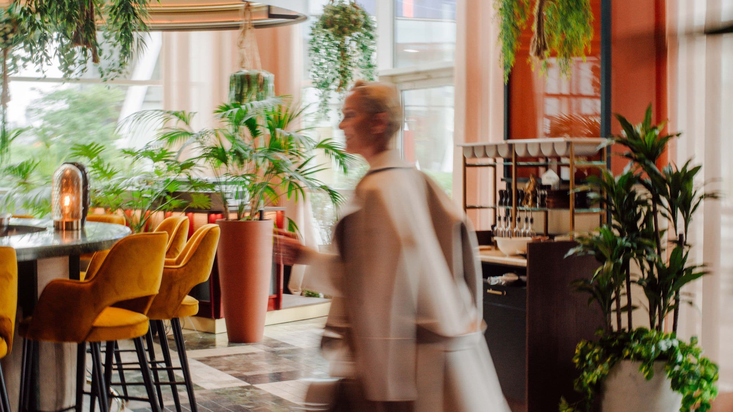 Stilvolle Hotel-Bar mit grüner Dekoration und Hockern, in der eine Frau entspannt den Raum durchquert