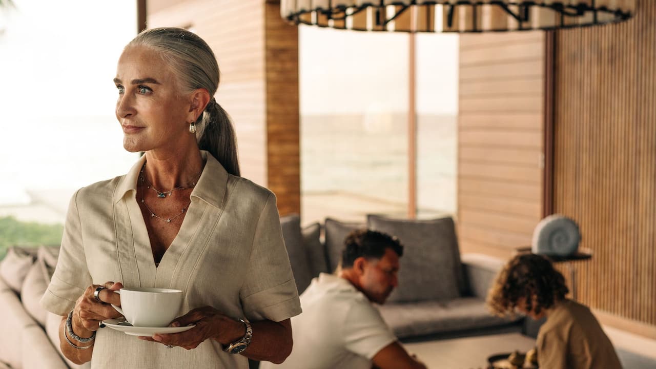 Park Hyatt Maldives Lady Holding Cup with Family Playing Behind