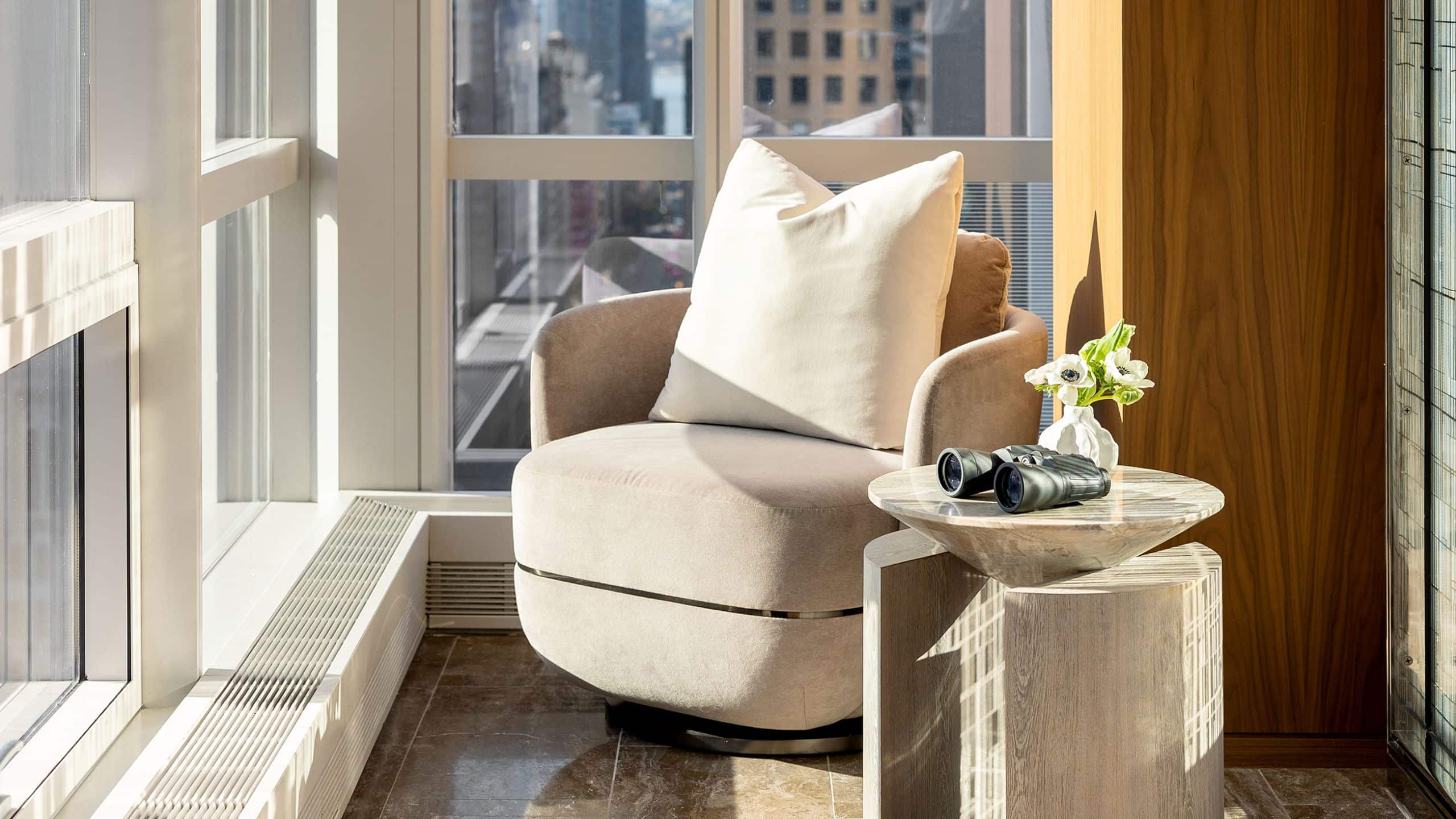 Corner suite reading nook with single velvet chair, marble side table, and views of New York
